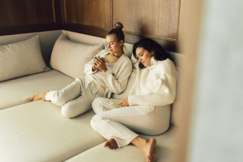 Zu sehen sind 2 Frauen auf einer großen, gemütlichen Couch sitzend, die ihre Zeit im Alpgues im Posthotel Taube genießen.