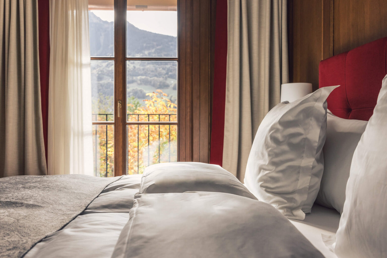 Detailaufnahme Des Doppelbettes inklusive Blick auf des Bergpanorama durch das Fenster im Hintergrund.