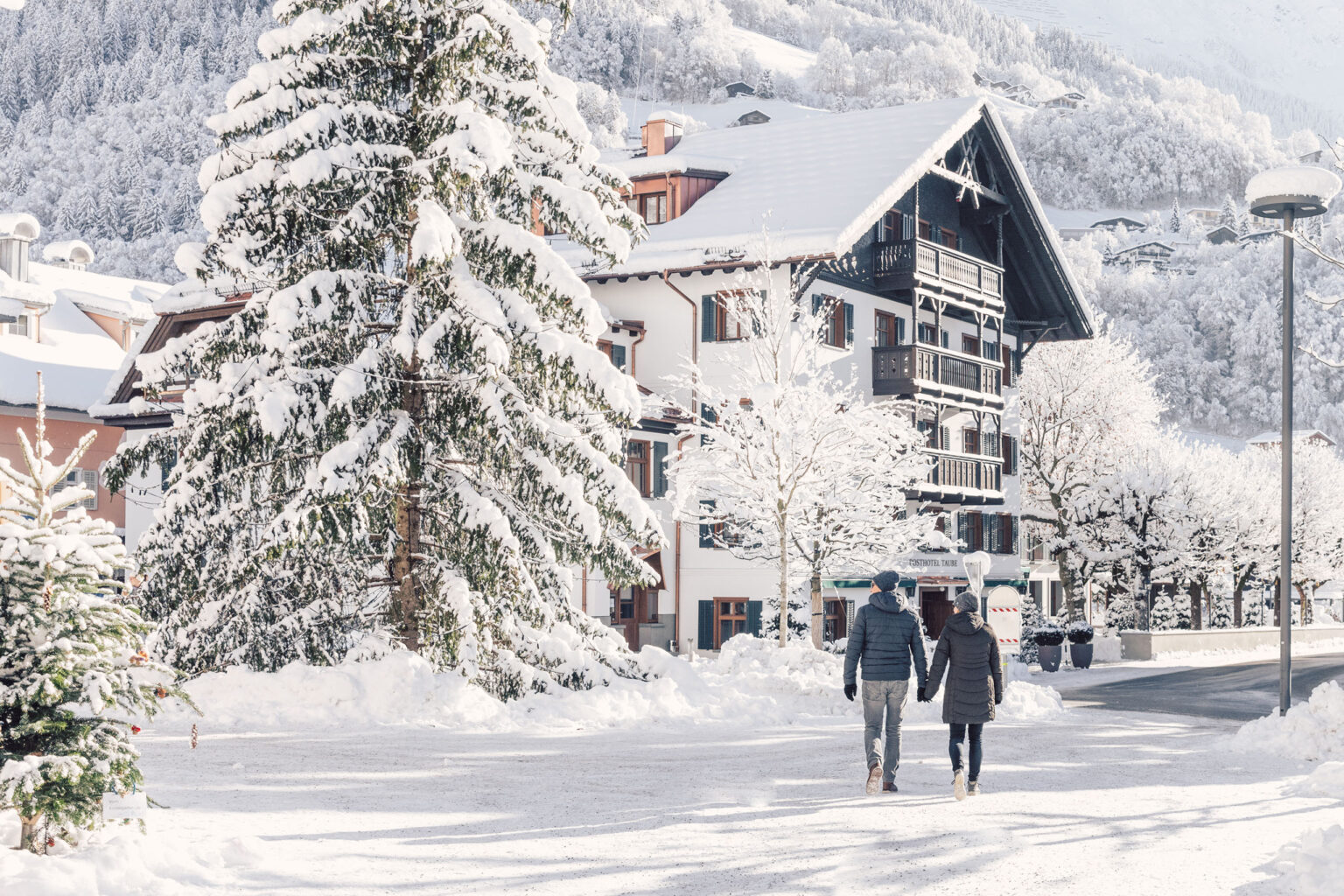 Außenansicht im Winter, Paar spaziert im Schnee – Posthotel Taube in Schruns